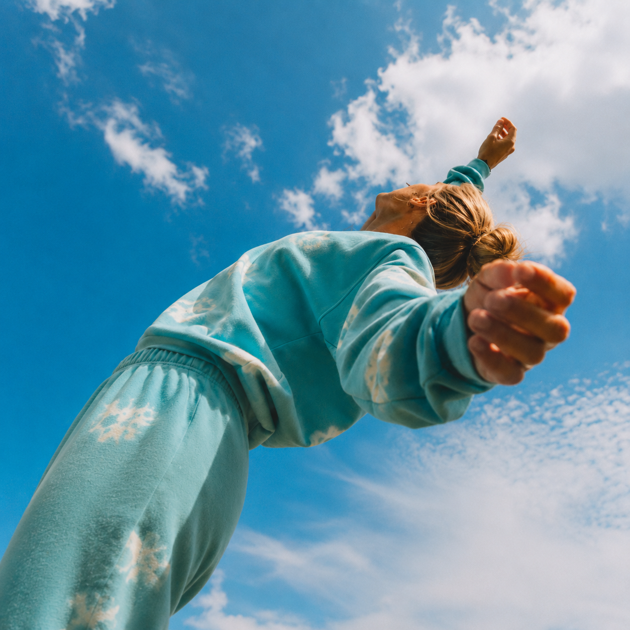 A person in blue-green Trees clothing reaching toward the sky
